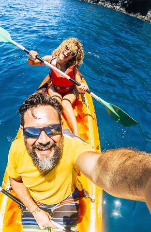 A happy couple taking a selfie while kayaking in deep blue ocean waters during a customized vacation.