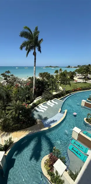 Luxury all-inclusive resort pool overlooking a tropical beach with turquoise water and palm trees.