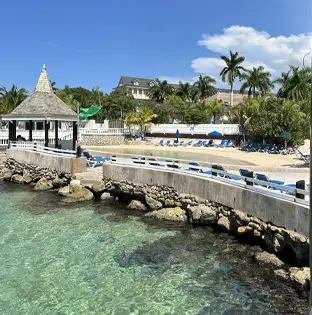 Seaside gazebo and lounge chairs along a rocky shoreline with clear turquoise water at a tropical resort.