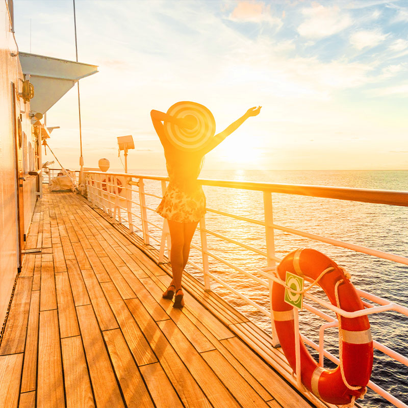 A traveler in a sun hat enjoying a golden sunset from the wooden deck of a luxury cruise ship