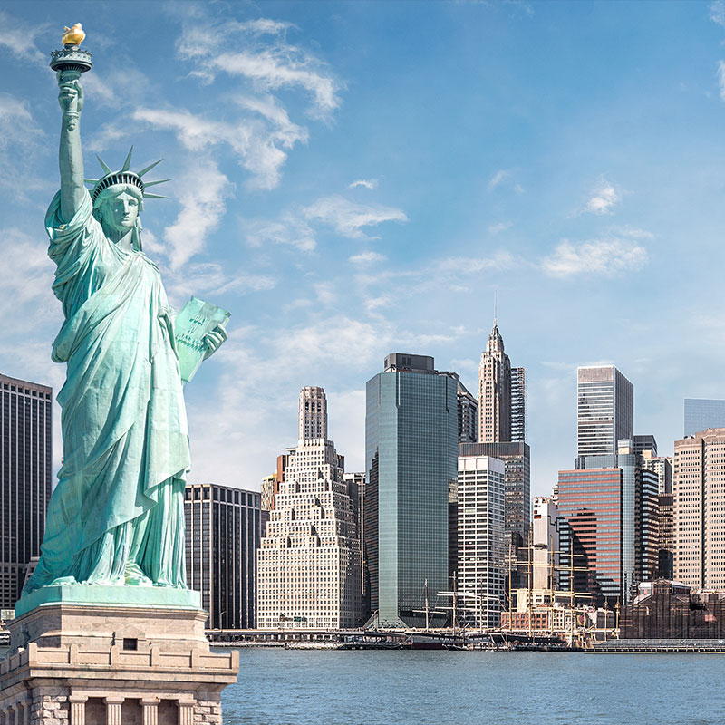 The Statue of Liberty standing tall against the iconic New York City skyline under a clear blue sky.