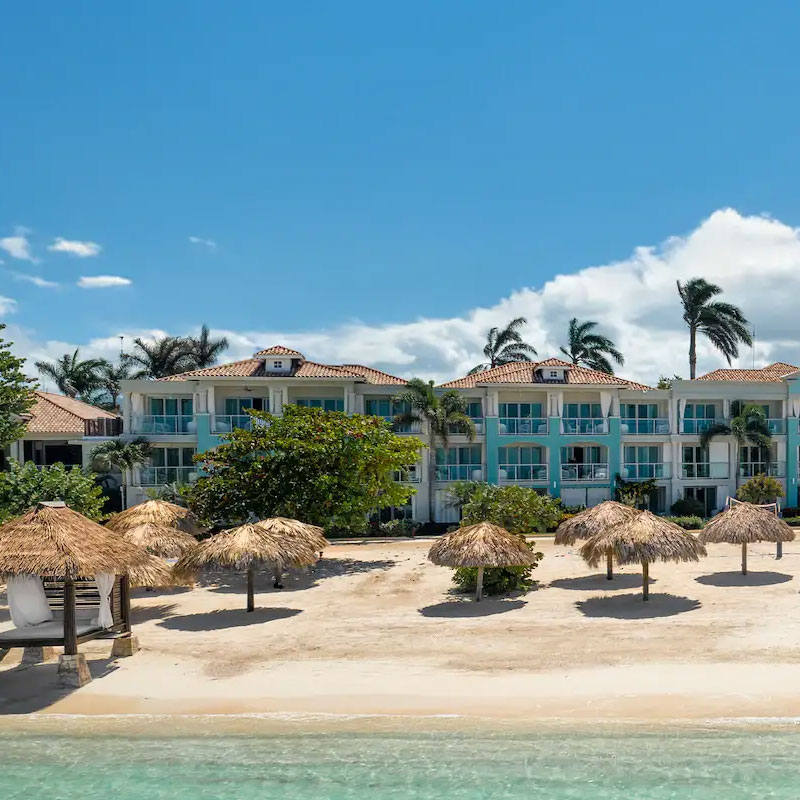 Luxury all-inclusive beachfront resort with turquoise buildings and straw umbrellas on a private white sand beach.